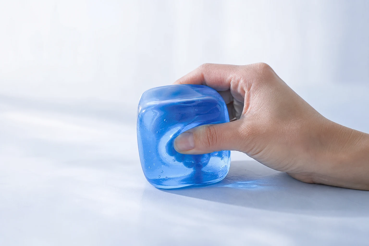 Illustrative close-up of a hand slowly pressing a translucent blue rounded sensory cube